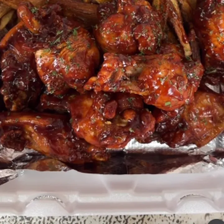 Glazed red-sauced chicken wings over fries in a takeout box