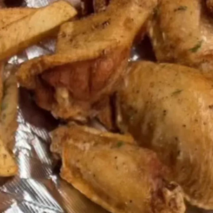 Seasoned fried chicken wings next to thick-cut fries on foil